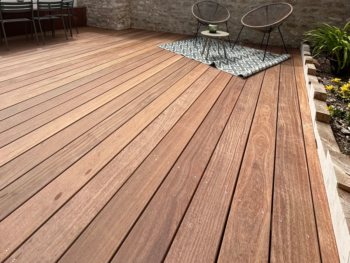 Terrasse en bois aménagée devant un mur en pierre
